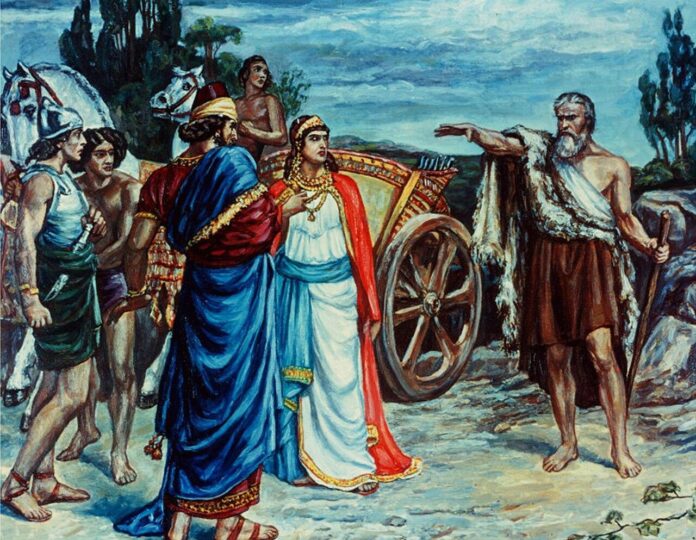 1280px-Jezabel-and-Ahab-Meeting-Elijah-in-Naboth-s-Vineyard Jezabel i Achab spotykają proroka Eliasza w winnicy Nabota – kolorowa rycina Francisa Dicksee'ego, ukazująca starca w płaszczu ze zwierzęcej skóry, który oskarżycielsko wskazuje na króla i królową stojących przy rydwanie (domena publiczna, Wikimedia Commons)