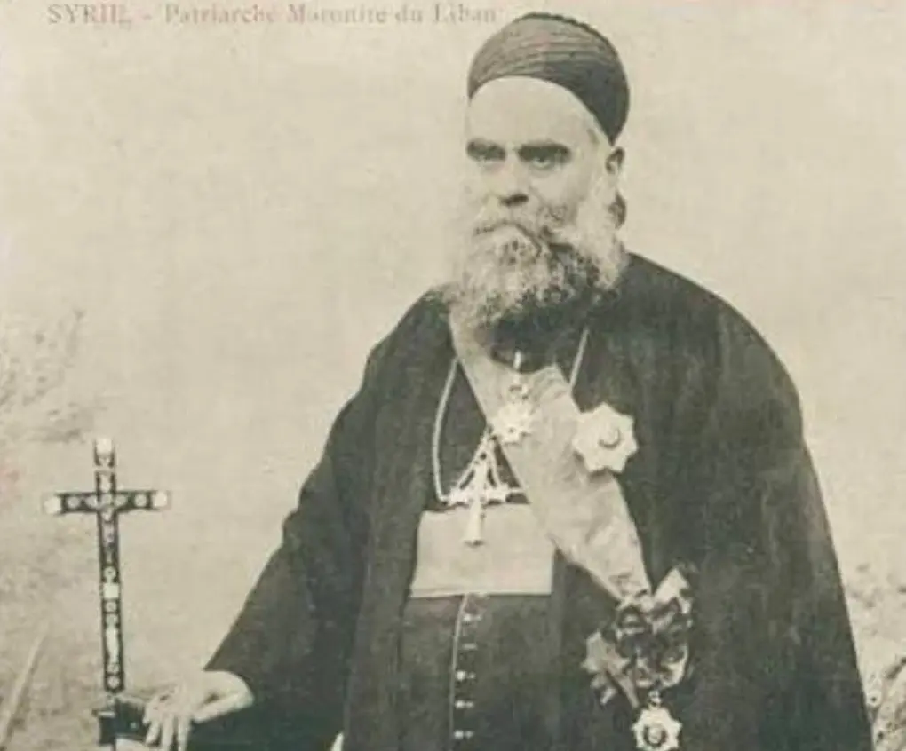Howayek Archiwalna fotografia patriarchy maronickiego Eliasza Hoyeka w szatach liturgicznych, z krzyżem i orderami, stojącego obok krucyfiksu