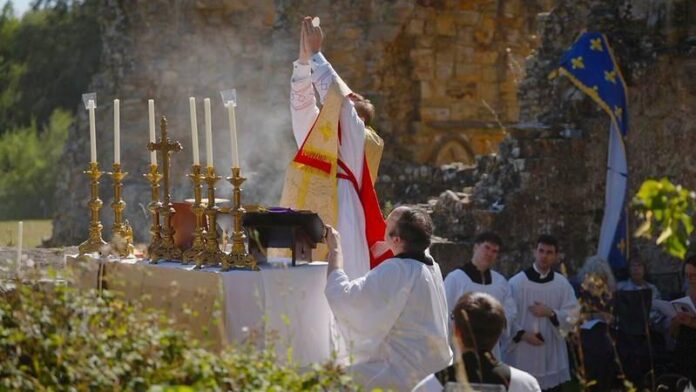abadia-de-bayham Kapłan unosi w górę Hostię podczas Podniesienia w czasie Mszy Świętej w tradycyjnym rycie rzymskim, odprawianej na wolnym powietrzu wśród ruin opactwa Bayham, przy ołtarzu ze złotymi lichtarzami.