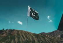Porwanie nieletniej w Pakistanie wstrząsa krajem: sąd oddaje dziewczynkę porywaczowi Flaga Pakistanu powiewa na maszcie na tle błękitnego nieba i wzgórz (fot. Ali Khokhar, Unsplash)