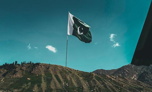ali-khokhar-TlC4DzclSN8-unsplash-1 Flaga Pakistanu powiewa na maszcie na tle błękitnego nieba i wzgórz (fot. Ali Khokhar, Unsplash)