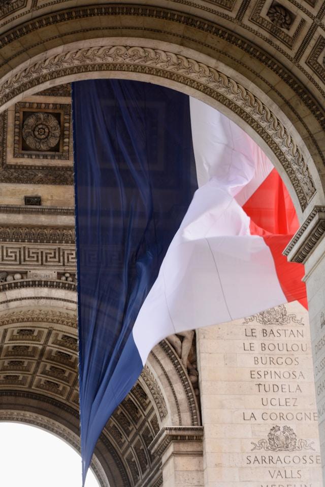 cecilia-miraldi-o2AB8IzHYPQ-unsplash-1 Wielka flaga Francji zawieszona pod łukiem Arc de Triomphe w Paryżu, symbol jedności narodowej