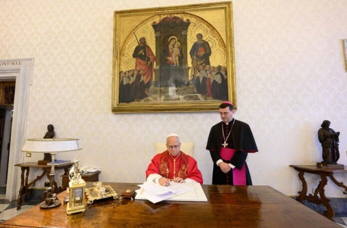 Papież Leon XIV podpisuje encyklikę Magnifica humanitas przy biurku w Watykanie, w obecności biskupa