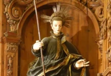 Święty Jan Berchmans: młody jezuita, który pozostawił woń świętości Figura świętego Jana Berchmansa w czarnej jezuickiej sutannie ze złoceniami, z aureolą promieni wokół głowy, trzymającego laskę, w rzeźbionej niszy