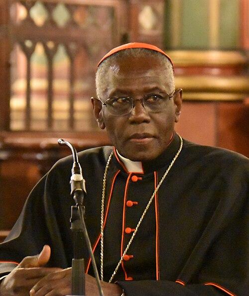 500px-Cardinal_Robert_Sarah_cropped-1 Kard. Robert Sarah w czarnej sutannie z czerwonymi wypustkami i piusce, przy mikrofonie we wnętrzu kościoła — zdjęcie archiwalne, nie z omawianego wywiadu.