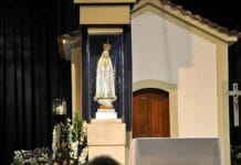 Czwarte objawienie fatimskie w Valinhos: przesłanie, które przetrwało ponad sto lat Ukoronowana figura Matki Bożej Fatimskiej w białej szacie na cokole przed granatowym tłem, obok białej Kaplicy Objawień z krucyfiksem; u stóp lilie i ołtarz.