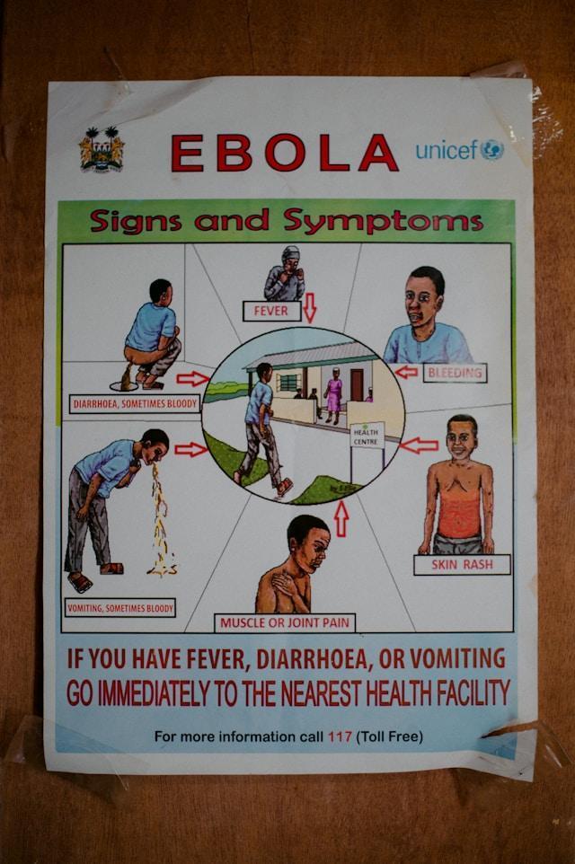 Ebola-Poster Plakat UNICEF o objawach eboli przyklejony taśmą do drewnianej ściany; rysunki pokazują gorączkę, wymioty, biegunkę i wysypkę oraz apel o wizytę w przychodni