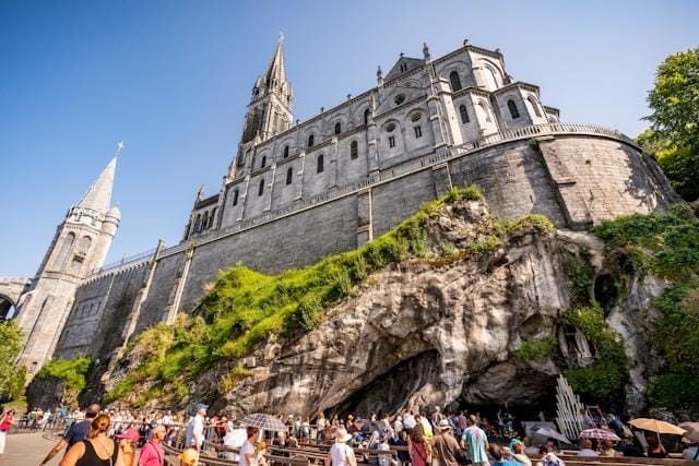 Lourdes Bazylika Niepokalanego Poczęcia i Bazylika Różańcowa wznoszące się nad skałą Massabielle w Lourdes, z pielgrzymami zgromadzonymi przed grotą u ich stóp
