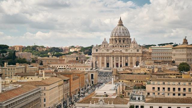 Vatican-City-St-Peters-Basilica Bazylika Świętego Piotra w Watykanie z charakterystyczną kopułą, widziana ponad dachami budynków Rzymu pod zachmurzonym niebem