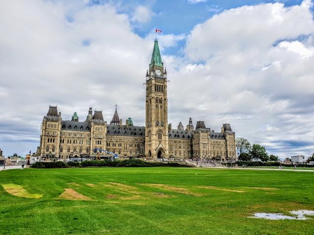benoit-debaix-ReUoz0CwfGo-unsplash Wzgórze Parlamentarne (Parliament Hill) w Ottawie – gmach parlamentu Kanady z Wieżą Pokoju i kanadyjską flagą na tle zachmurzonego nieba