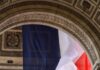 Czy ataki na symbole katolickie we Francji są bagatelizowane jako zwykła kontrowersja? Francuska flaga trójkolorowa zawieszona pod sklepieniem Łuku Triumfalnego w Paryżu, obok wyrytych nazw bitew