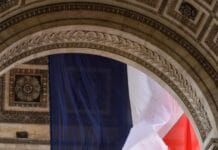 Czy ataki na symbole katolickie we Francji są bagatelizowane jako zwykła kontrowersja? Francuska flaga trójkolorowa zawieszona pod sklepieniem Łuku Triumfalnego w Paryżu, obok wyrytych nazw bitew