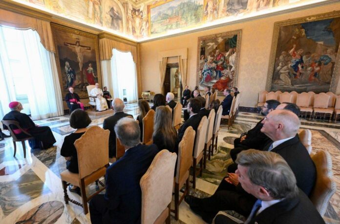 Papież Leon XIV podczas audiencji w watykańskiej sali przyjmuje delegację Towarzystwa Świętego Wincentego a Paulo; obok niego biskup, przed nimi rzędy gości.