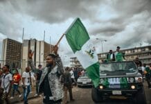 Ataki pasterzy Fulani: dziesiątki zabitych chrześcijan w trzech stanach Nigerii Mężczyzna trzyma dużą nigeryjską flagę podczas ulicznego zgromadzenia w Port Harcourt w Nigerii; w tle tłum i terenowy samochód udekorowany flagami