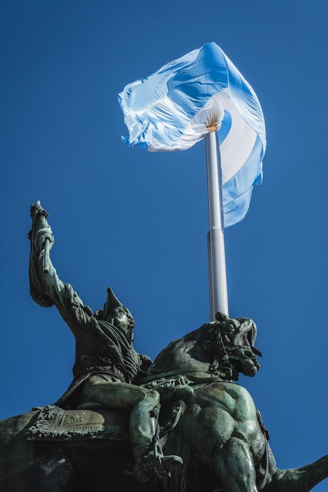 Dzień Akcji za Dwa Życia jednoczy grupy pro-life w Argentynie i Meksyku Brązowy pomnik konny — jeździec z uniesionym ramieniem; nad nim biało-błękitna flaga Argentyny ze Słońcem Majowym na tle bezchmurnego nieba.