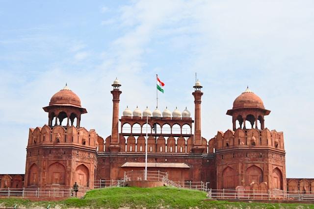 jayanth-muppaneni-_ymJkgX4Vhw-unsplash Czerwony Fort (Lal Qila) w Delhi w Indiach z powiewającą indyjską flagą narodową na tle błękitnego nieba