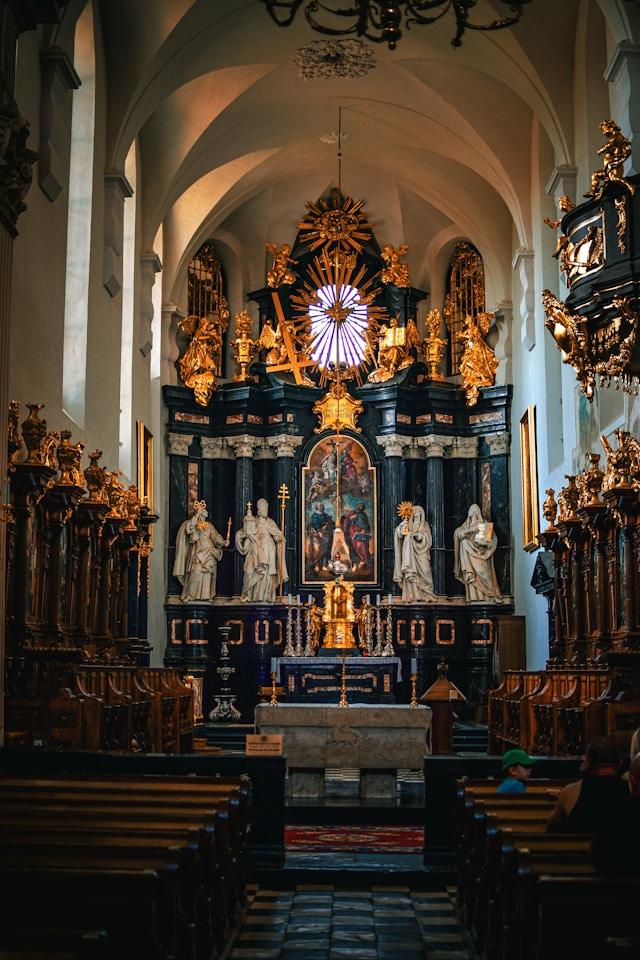 nathan-lilly-DpKifm4UUj4-unsplash Barokowy ołtarz główny z pozłacanymi rzeźbami i obrazem w kościele opactwa benedyktynów w Tyńcu w Krakowie. Zdjęcie ilustracyjne.
