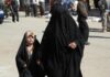 Irak: sąd przywrócił chrześcijańską tożsamość, wraca spór o dzieci konwertytów Kobieta w czarnej abai prowadzi za rękę dziewczynkę w kwiecistej chuście przez ulicę irackiego miasta; w tle przechodnie i żołnierz