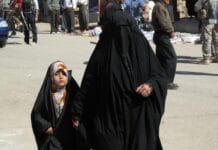 Irak: sąd przywrócił chrześcijańską tożsamość, wraca spór o dzieci konwertytów Kobieta w czarnej abai prowadzi za rękę dziewczynkę w kwiecistej chuście przez ulicę irackiego miasta; w tle przechodnie i żołnierz