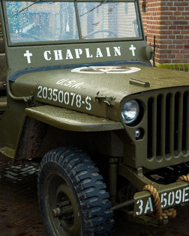 willy-the-wizard-mo1Nex0LOnU-unsplash Zabytkowy wojskowy jeep w kolorze khaki z białym napisem „CHAPLAIN” i dwoma krzyżami na masce, symbol kapelana wojskowego