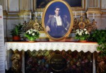 Rok po kanonizacji: pierwszy międzynarodowy Szlak Frassatiego otwarty w Portugalii Grób św. Pier Giorgia Frassatiego w katedrze w Turynie: owalny portret nad ołtarzem, świeczniki, białe kwiaty i tablica „Beato Pier Giorgio Frassati”.