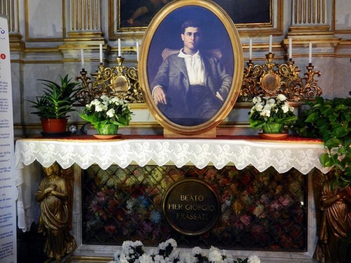 Grób św. Pier Giorgia Frassatiego w katedrze w Turynie: owalny portret nad ołtarzem, świeczniki, białe kwiaty i tablica „Beato Pier Giorgio Frassati”.