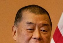 Jimmy Lai znów w centrum uwagi przed szczytem Trumpa z Xi Jimmy Lai, siwiejący mężczyzna w jasnej marynarce, prążkowanej koszuli i czerwonym krawacie, mówi coś; w tle beżowa ściana i amerykańska flaga.