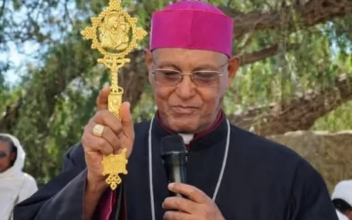 Biskup Tesfaselassie Medhin z eparchii Adigrat w Etiopii przemawia na zewnątrz, trzymając ozdobny krzyż ręczny i mikrofon.