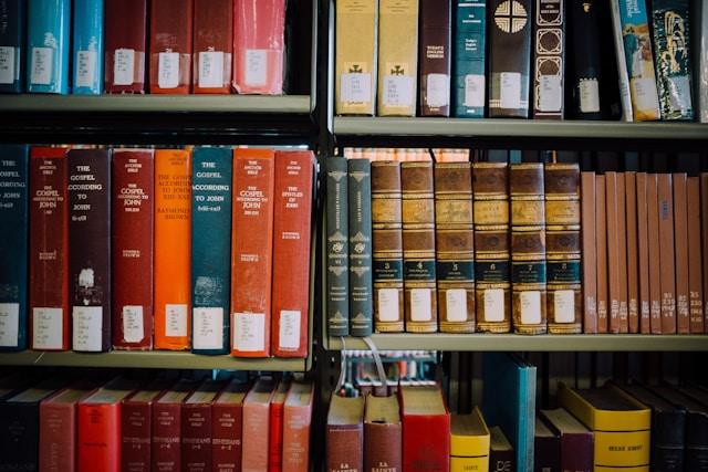 books-on-theology Regały biblioteczne wypełnione komentarzami do Ewangelii św. Jana i księgami teologicznymi w czerwonych, brązowych i niebieskich oprawach