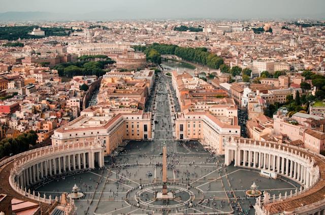 caleb-miller-0Bs3et8FYyg-unsplash Widok z lotu ptaka na plac św. Piotra w Watykanie: centralny obelisk, półkoliste kolumnady i Via della Conciliazione biegnąca w stronę Rzymu.