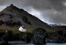Islandia: nowy kościół w Selfoss to dziewiąta wspólnota katolicka w kraju Islandzki krajobraz: biały dom z czerwonym dachem u stóp góry nad skalistym wybrzeżem. Zdjęcie ilustracyjne, nie przedstawia kościoła w Selfoss.