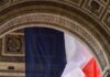 Wizyta Leona XIV we Francji pod maksymalną ochroną wobec zagrożenia dżihadystycznego Ilustracyjne zdjęcie archiwalne: wielka flaga Francji zawieszona pod sklepieniem Łuku Triumfalnego w Paryżu, obok kamiennych tablic z nazwami bitew.