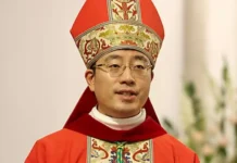 Nowy arcybiskup Chongqing wyświęcony w Chinach w ramach umowy ze Stolicą Apostolską Duchowny w czerwonym ornacie i mitrze biskupiej podczas liturgii, w tle białe kwiaty — zdjęcie ilustrujące święcenia biskupie w Chongqing.