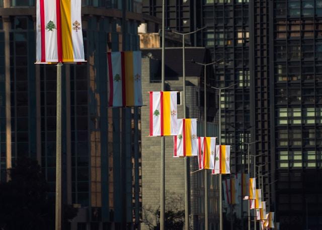 christian-harb-qP5wI976gyI-unsplash Flagi Libanu i Watykanu zawieszone na latarniach wzdłuż ulicy, w tle szklane wieżowce. Zdjęcie ilustracyjne, nie z wiosek przygranicznych.
