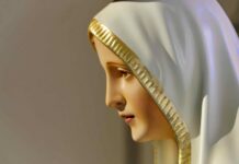Kryzys wiary a orędzie fatimskie Zbliżenie profilu figury Matki Bożej Fatimskiej w białym welonie ze złotą lamówką, z lekko pochyloną głową, na jasnym, rozmytym tle
