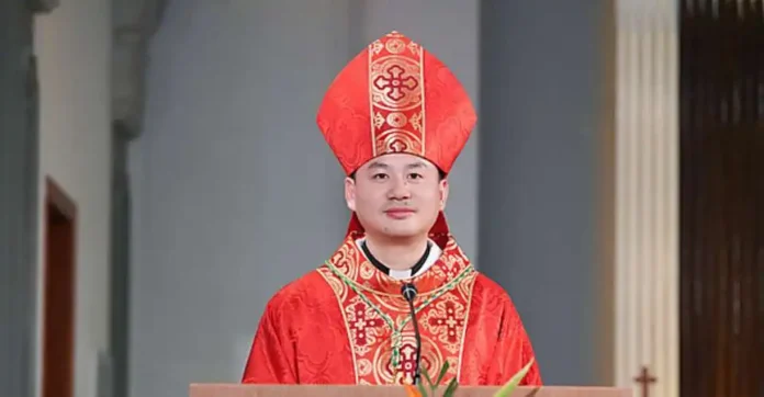 check-china-ordains-new-haimen-bishop-under-vatican-agreement-6ad1f98d420e0_600 Młody biskup w czerwonej mitrze i czerwono-złotym ornacie stoi przy ambonie z mikrofonem w jasnym wnętrzu kościoła