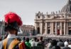 Spotkanie w Watykanie o „Amoris laetitia”: od dawnych sporów do towarzyszenia rodzinom Gwardzista szwajcarski w hełmie z czerwonym pióropuszem, w tle tłum wiernych na placu św. Piotra i fasada bazyliki watykańskiej