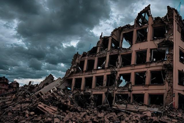norman-koroliuk-PH9S5SfpV0E-unsplash Zniszczony, częściowo zawalony wielopiętrowy budynek i sterty gruzu pod ciemnym, burzowym niebem – zdjęcie ilustracyjne